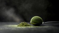 Green matcha ice cream scoop on silver spoon with powdered tea scattered on dark background, dramatic moody food photography with atmospheric lighting.