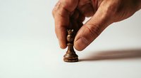 Male hand with medium skin tone positioning wooden chess pawn on white surface, strategy and planning concept for business, leadership, and decision-making themes.