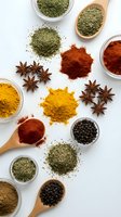 Colorful spices and herbs collection with turmeric, paprika, star anise, black pepper and dried herbs in bowls and wooden spoons on white background.