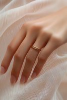 Elegant female hand wearing minimalist gold ring against flowing white fabric background, soft natural lighting creates gentle shadows and romantic atmosphere.