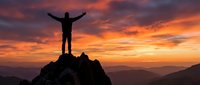 Male hiker silhouette celebrating success on mountain peak at dramatic sunset with arms raised against colorful sky and mountain ranges.