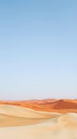 Vast desert landscape with rolling sand dunes in warm golden and orange tones beneath clear blue sky, suitable for travel and nature backgrounds.