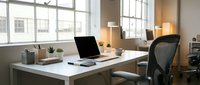 Modern home office workspace with white desk, open laptop, black ergonomic chair, and natural light from large windows, suitable for remote work and business concepts.