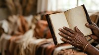 Hands of an older adult with dark skin tone holding an open book with blank pages, suitable for education, literacy, reading, and learning concepts.