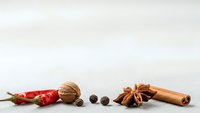 Aromatic spices and ingredients arranged on neutral background including cinnamon stick, star anise, walnut, peppercorns and red chili peppers.