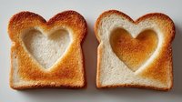 Heart-shaped cutouts in toasted bread slices on neutral background, showing contrast between golden-brown edges and soft white interior.