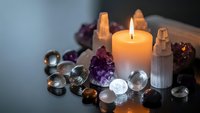 Burning candle surrounded by amethyst crystals, selenite towers and glass spheres creating peaceful meditation and spiritual healing atmosphere.