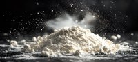 White flour explosion with floating particles against dark background creating dramatic culinary scene with natural lighting and powder movement effect.