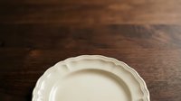 Elegant white ceramic plate with decorative rim on dark wooden surface, suitable for tableware, dining, and home decor design projects.