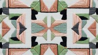 Geometric embroidery pattern with coral pink and sage green threads creating symmetrical kaleidoscope design on white fabric background.