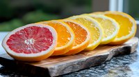 Fresh citrus fruit slices arranged in gradient color from pink grapefruit to orange and lemon on rustic wooden board, healthy vitamin C food concept.
