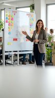 Professional businesswoman presenting project strategy on whiteboard with colorful sticky notes in modern office environment for team collaboration.