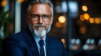 Confident mature businessman with gray beard and glasses smiling in modern office environment with warm bokeh lighting for corporate presentations.