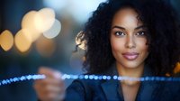 Young African American businesswoman with natural curly hair smiling confidently against blurred bokeh lights background, professional corporate portrait.
