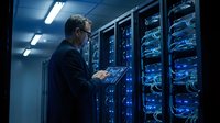IT administrator monitoring server room with laptop checking network infrastructure and data center equipment for system maintenance and troubleshooting.