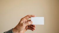 Close-up of male hand holding blank white business card against neutral beige background, suitable for branding, corporate identity, and marketing mockup designs.