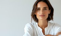 Young Caucasian woman with brown hair wearing white button-up shirt against light background, looking at camera with natural makeup and confident expression. Professional portrait.