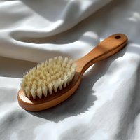 Natural wooden massage brush with soft bristles on white textile background with gentle shadows and folds, spa wellness concept.