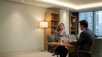 Two professionals engaged in a business meeting in a modern office setting with wooden furniture and city views.