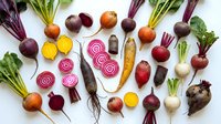 Fresh organic beetroot varieties with colorful roots and green leaves arranged on white background for healthy cooking recipes.