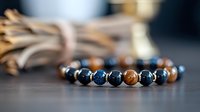 Elegant beaded bracelet with blue and brown natural stone beads separated by metallic spacers on wooden surface, selective focus creates artistic jewelry composition.