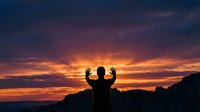Silhouetted male figure with arms raised in celebration against dramatic golden and purple sunset sky with mountain landscape backdrop.