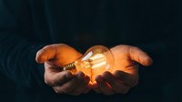 Hands holding glowing incandescent light bulb against dark background, symbolizing innovation, ideas, creativity, and sustainable energy solutions for business and technology concepts.