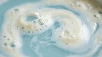 Swirling blue and white soap foam creates abstract patterns with bubbles in creamy lather texture for skincare and cleaning product concepts.