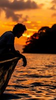 Young man with curly dark hair, sitting on driftwood by the ocean at golden hour sunset, silhouetted against warm orange and yellow sky, contemplative mood, peaceful coastal scene.