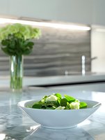 Fresh green salad with mozzarella cheese in white bowl on marble kitchen counter. Healthy eating and cooking concept for restaurants and home dining.