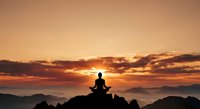 Person silhouette meditating on mountain peak at sunrise with dramatic orange sky and layered mountain ranges creating peaceful spiritual atmosphere.