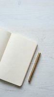 Open notebook with grid pages and gold pen on white wooden surface, ready for writing, planning, and creative work.