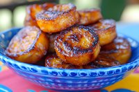 Caramelized plantains served in traditional blue ceramic bowl, golden brown with crispy edges and soft center, sweet tropical dessert on colorful table setting.