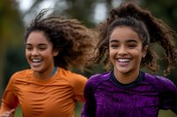 Two young African American women jogging together outdoors, smiling and enjoying their fitness routine in colorful athletic wear during daytime exercise.