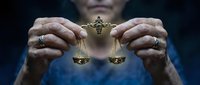 Hands holding golden scales of justice symbol representing law, legal system, fairness and judicial balance in courtroom or legal office setting.