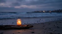 Glowing candle in glass jar on driftwood at twilight beach with ocean waves and distant lights creating romantic coastal atmosphere for relaxation concepts.