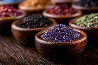 Aromatic dried tea leaves and flower petals in wooden bowls on rustic table, close up view of loose herbal blend with purple, pink and green varieties.