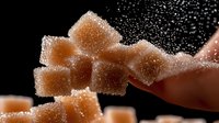 Brown sugar cubes with powdered sugar dust falling against black background, showcasing sweetness and texture for food photography.