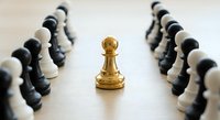 Golden chess pawn standing alone surrounded by fallen black and white chess pieces on wooden board representing leadership and victory in strategic game.