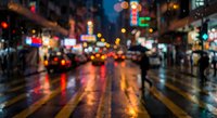 Blurred city street at night with colorful lights reflecting on wet pavement, creating bokeh effect. Urban nightlife and rainy weather atmosphere.