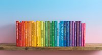 Colorful rainbow books arranged in spectrum order on wooden shelf against gradient blue to pink background for education and learning concepts.