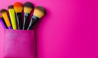 Professional makeup brushes in pink leather holder against vibrant magenta background with copy space. Beauty and cosmetics concept for social media and blogs.