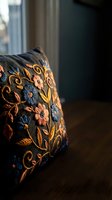 Ornate embroidered cushion with colorful floral patterns on dark fabric in cozy home interior setting for luxury decor and textile design projects.
