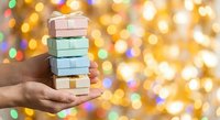 Hands holding stack of colorful gift boxes against festive bokeh lights background for holiday celebrations and present giving occasions.