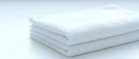 Soft white folded towels stacked on a light background, showcasing clean, fluffy texture for spa, hotel, or bathroom concepts.