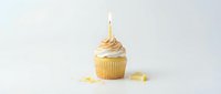Vanilla cupcake with golden frosting swirl, lit candle, and scattered gold confetti on white background for birthday celebrations and festive baking content.