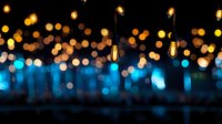Glowing vintage Edison bulbs hanging against blurred blue and golden bokeh background create atmospheric mood lighting for events and celebrations.