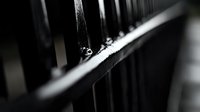 Dark metal fence bars in dramatic black and white macro photography with shallow depth of field creating abstract pattern of light and shadows. Prison concept.
