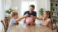 Happy Caucasian father teaching financial literacy to young children with pink piggy bank at home table, family money saving education concept.