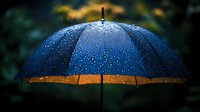 Blue umbrella with water drops against dark background, illuminated by warm light. Moody rainy weather atmosphere with bokeh effect and golden accents.